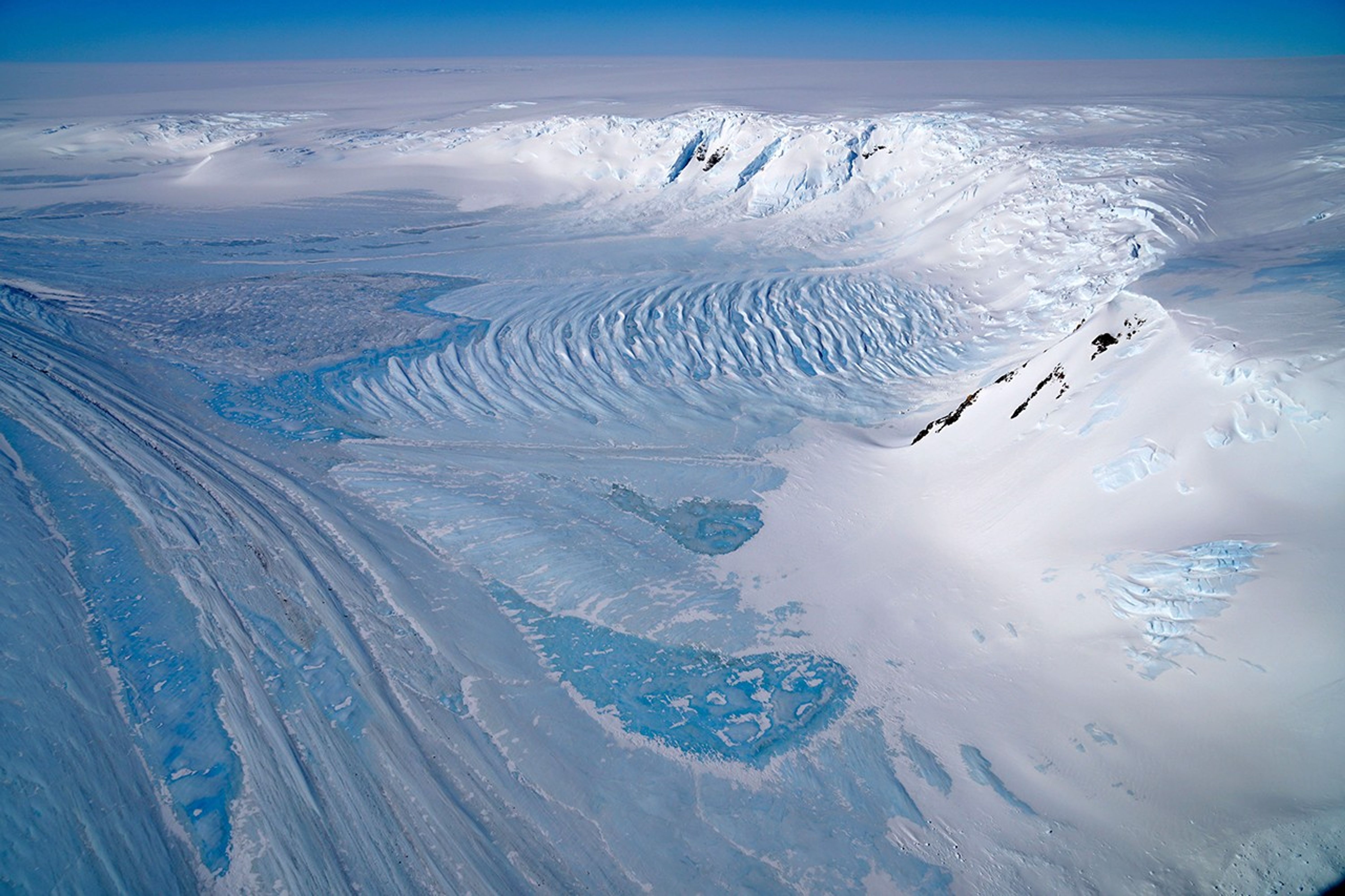 Blue ice flows between snow-covered ridges of Antarctica’s Transantarctic Mountains.